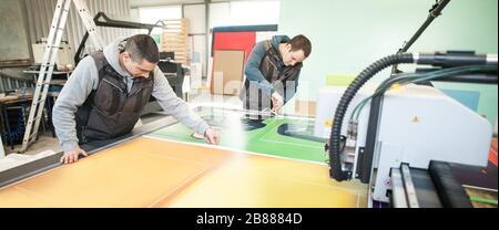 Two printshop worker technicians works on large CNC computer numerical control printing and cutting machine Stock Photo