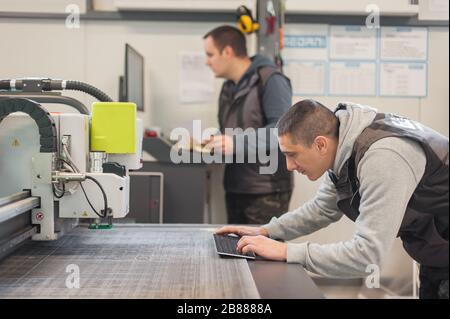 Two printshop worker technicians works on large CNC computer numerical control printing and cutting machine Stock Photo