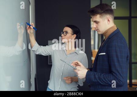 Young businesswoman writing on whiteboard and preparing report together with her colleague before the presentation at office Stock Photo