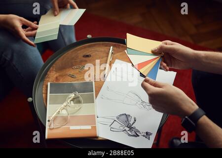 Close-up of team of designers looking at sketches and patterns and discussing new fashion collection together Stock Photo