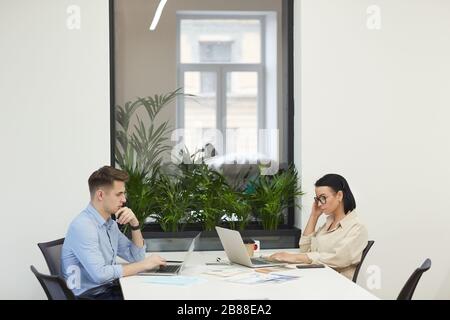 Young business colleagues sitting opposite each other at the table and working on laptop computers at office Stock Photo