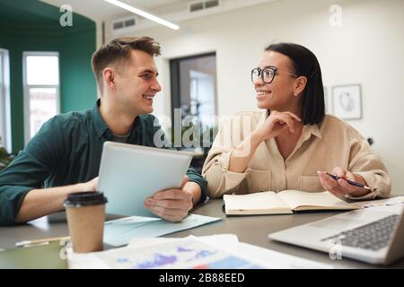 Two business colleagues sitting at the table and talking to each other while planning work in team at business meeting Stock Photo