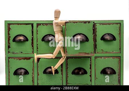 a wooden doll hanging on an open drawer of a small chest of drawers  looking for something Stock Photo