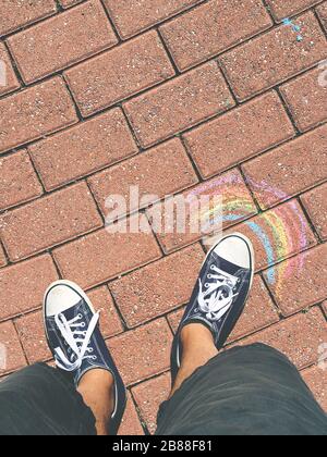 Sneakers on the road with a rainbow drawn. Spring and summer concept. Outdoor ideas and creativity. Stock Photo