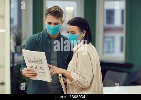 Two colleagues wearing protective masks standing at office and they discussing financial document Stock Photo