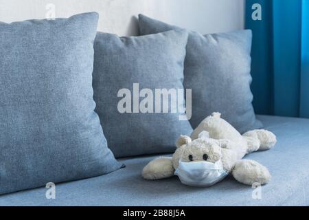 soft teddy bear lying on sofa in living room with medical mask on Stock Photo