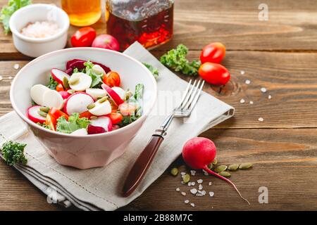 Salad from Iceberg lettuce, Kale and Radiccio, cherry tomatoes, radish, mini mozzarella and pumpkin seeds in bowls on dark wooden background Stock Photo