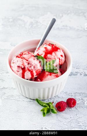 Raspberry ice cream balls with syrup, berries and mint leaves in white bowl Stock Photo