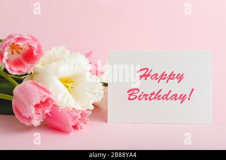 Happy Birthday text on gift card in flower bouquet. Beautiful bouquet of fresh flowers tulips with greeting card Happy Birthday on pink background. Stock Photo