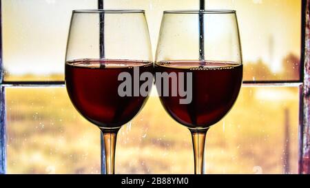 two glasses of red wine on the windowsill and rainy window background, autumn home time Stock Photo