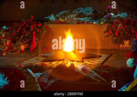 Close-up fire burns from the monument in the form of a star in honor of Victory Day in the war surrounded by numerous bouquets. Concept of memory of t Stock Photo