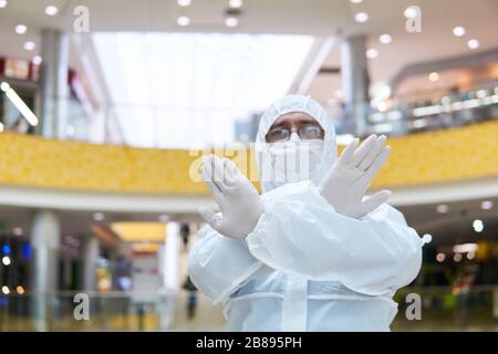 man in coverall disposable anti-epidemic antibacterial isolation suit shows a definitive stopping gesture with two hands against the background of som Stock Photo