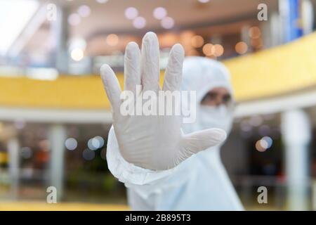 man in coverall disposable anti-epidemic antibacterial isolation suit shows a definitive prohibition gesture against the background of some interior o Stock Photo