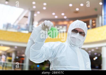 man in coverall disposable anti-epidemic antibacterial isolation suit suspiciously holds in his hand a rubber ball resembling a macro photo of a virus Stock Photo