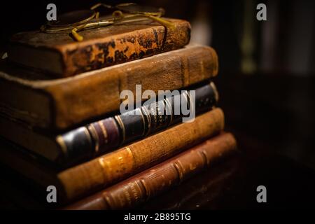 A vintage pile of three old brown leather books with eye glasses on a wood table. Stock Photo