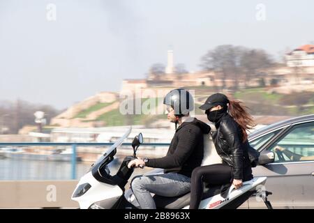 Belgrade, Serbia - March 19, 2020 : A couple riding on a scooter with a dog in the middle on the highway bridge, with Kalemegdan fortress behind them Stock Photo