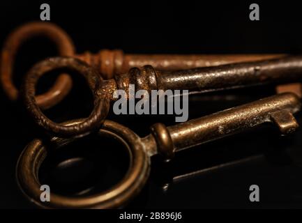 Group of 3 old metal keys, rusty and brown, on black background with soft reflections Stock Photo