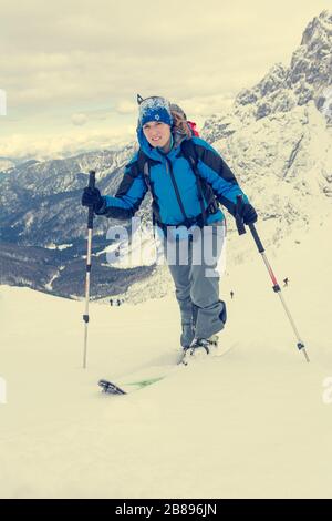 Female ski tourer ascending snow covered mountain slope. Stock Photo