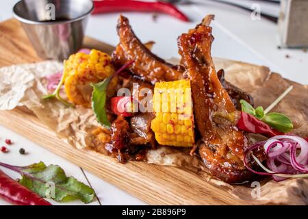Glazed pork ribs baked in soy sauce served with corn on a wooden board, horizontal format Stock Photo