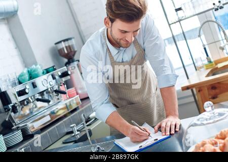 Young adult barista working in cafeteria, making notes Stock Photo