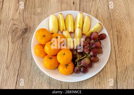 Apples, oranges, grapes on a white plate on a wooden table Stock Photo