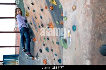 Little girl smiles as she poses while climbing an indoor rock wall at a kids play place Stock Photo