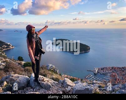 Happy smiling female traveler enjoying view of Dubrovnik old town from above at sunset time, Adriatic sea of Croatia Stock Photo