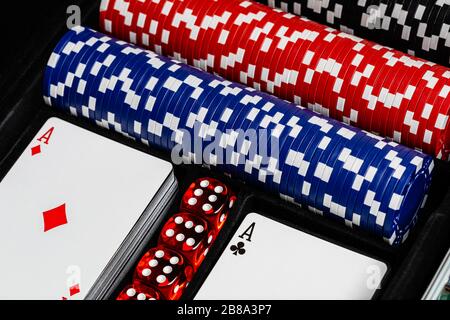 A case of betting chips in red, blue and black alongside 2 standard decks of cards showing an Ace of Diamonds and of Clubs with a row of 4 dice Stock Photo