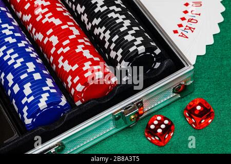 Black, Red and Blue betting chips in a case on a green felt playing surface with cards fanned on the table and a pair of casino style red dice beside Stock Photo