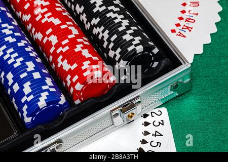 Black, Red and Blue betting chips in a case on a green felt playing surface with cards fanned on the table beside the case.  Some room for copy Stock Photo