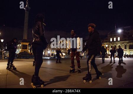 Trafalgar Square, London, UK. 20th March 2020. A group of rollerbladers enjoy empty streets, some of them wear surgical masks due to coronavirus; just after midnight on Saturday.  The government advises staying at home and limiting social life. Stock Photo