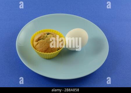 Quick on the run breakfast of blueberry muffin in silicone muffin cup and hard boiled egg on blue plate Stock Photo