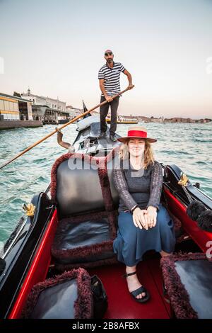 A woman posing for a picture on a gondola ride with the gondolier steering the boat in the background, Grand Canal, venice, Italy. Stock Photo