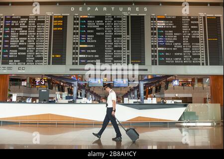 18.03.2020, Singapore, Republic of Singapore, Asia - A pilot walks past a flight information display in the departure hall at Changi Airport. Stock Photo