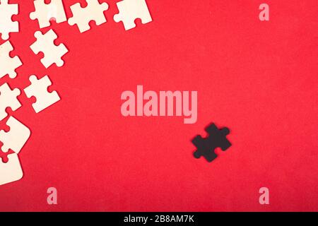 wooden white and black puzzles on a red background close-up top view. outcast antisocial leader differ from others children's educational toy. Stock Photo