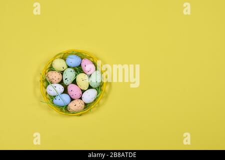 Multi-colored Easter eggs in a yellow basket on a yellow background. Place for an inscription. View from above. For postcards. Stock Photo