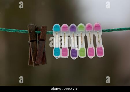 A group of colourful clothespin with two wooden ones hanging on a rope outdoors Stock Photo