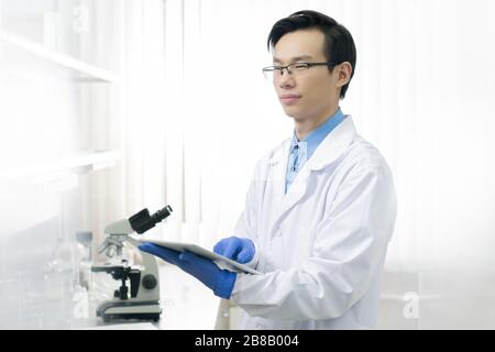 Young scientific researcher in workwear using touchpad to get online information about covid19 while studying it in laboratory Stock Photo