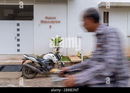 Pondicherry, India - March 17, 2018: An unrecognisable man passing in front of a nice residential building entrance on a bicycle with motion blur Stock Photo