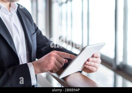 Business man using tablet by the window in modern glass office building. Businessman holding smart mobile device and working. Pressing touch screen. Stock Photo