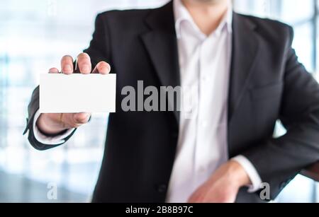 Casual business man holding empty white business card in modern office building. Free blank copy space. Stock Photo