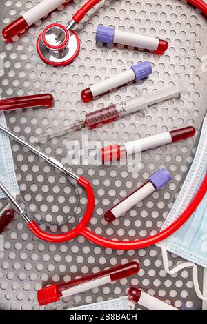 Blood sample along with syringe, protective mask and stethoscope on metal surface Stock Photo