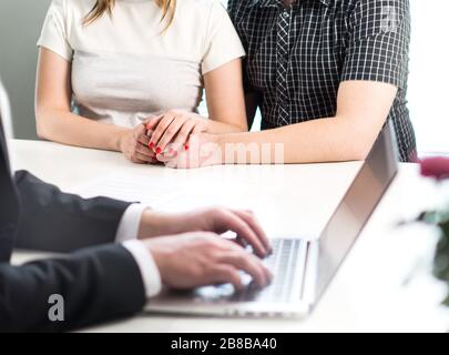 Couple holding hands in meeting with professional man using laptop. Adoption consultation, fertility clinic or financial guidance. Stock Photo