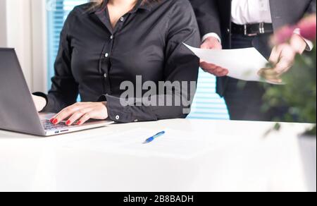 Team of lawyers or business people working together. Boss or executive manager holding and reading paper document while assistant is using laptop. Stock Photo
