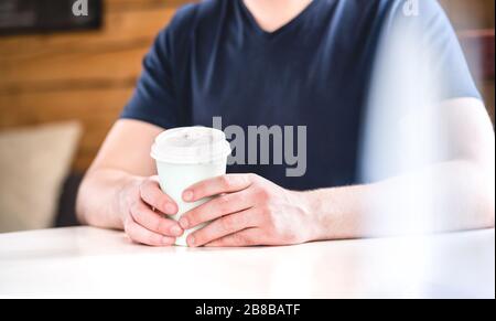 Man holding take away coffee cup in hands on table in cafe, coffee shop or home. Guy with hot chocolate or tea. Stock Photo