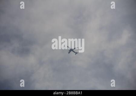 A single plane is seen from below as it tries to pass the thick clouds on a dark summer day Stock Photo