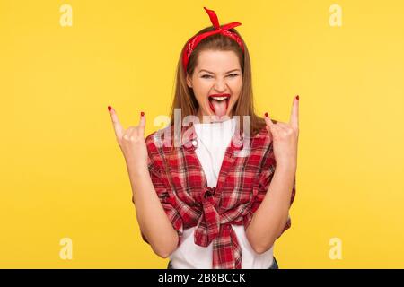 Portrait of unruly pinup girl in checkered shirt and headband making rock n roll punk gesture roaring crazy, showing tongue out. retro vintage 50's st Stock Photo