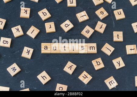 Autism spelled in wooden letter blocks with letters randomly spread around image  on dark slate background. Stock Photo