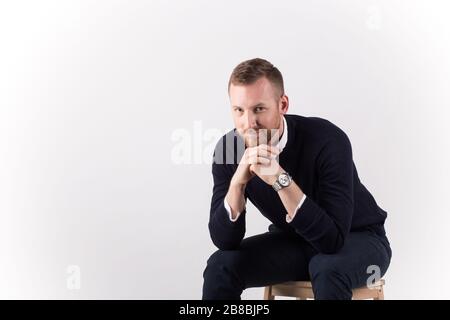 Image of handsome cheerful young man sitting and smiling isolated over white wall. Looking in the camera. Stock Photo