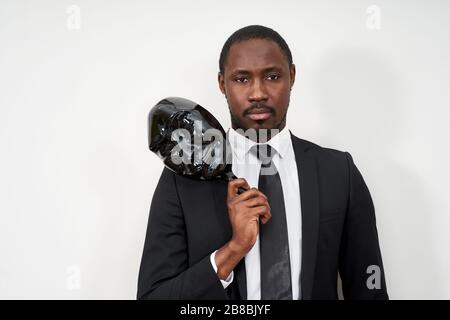 African young man wearing black suit taking off plastic mask revealing face Stock Photo